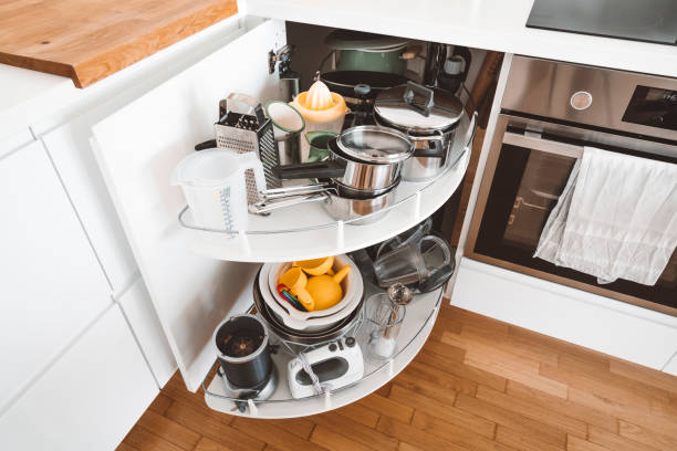 Corner cabinet in all white modern kitchen. Open cabinet with pots and pans.