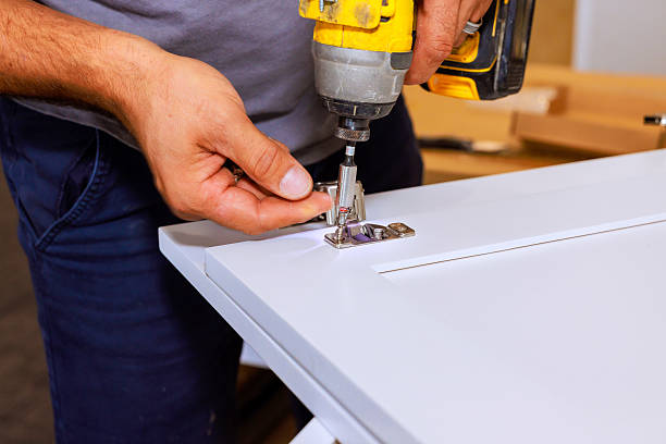 Installer uses screwdriver drill to attach hinges to cabinet door inside